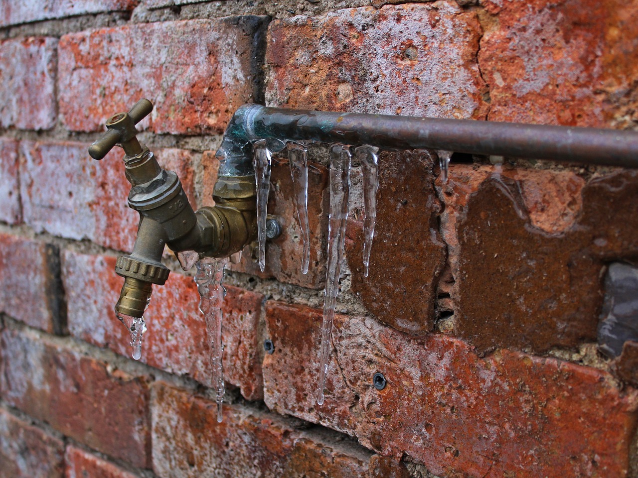 A brick wall with a spigot hanging out of it, covered in icicles.